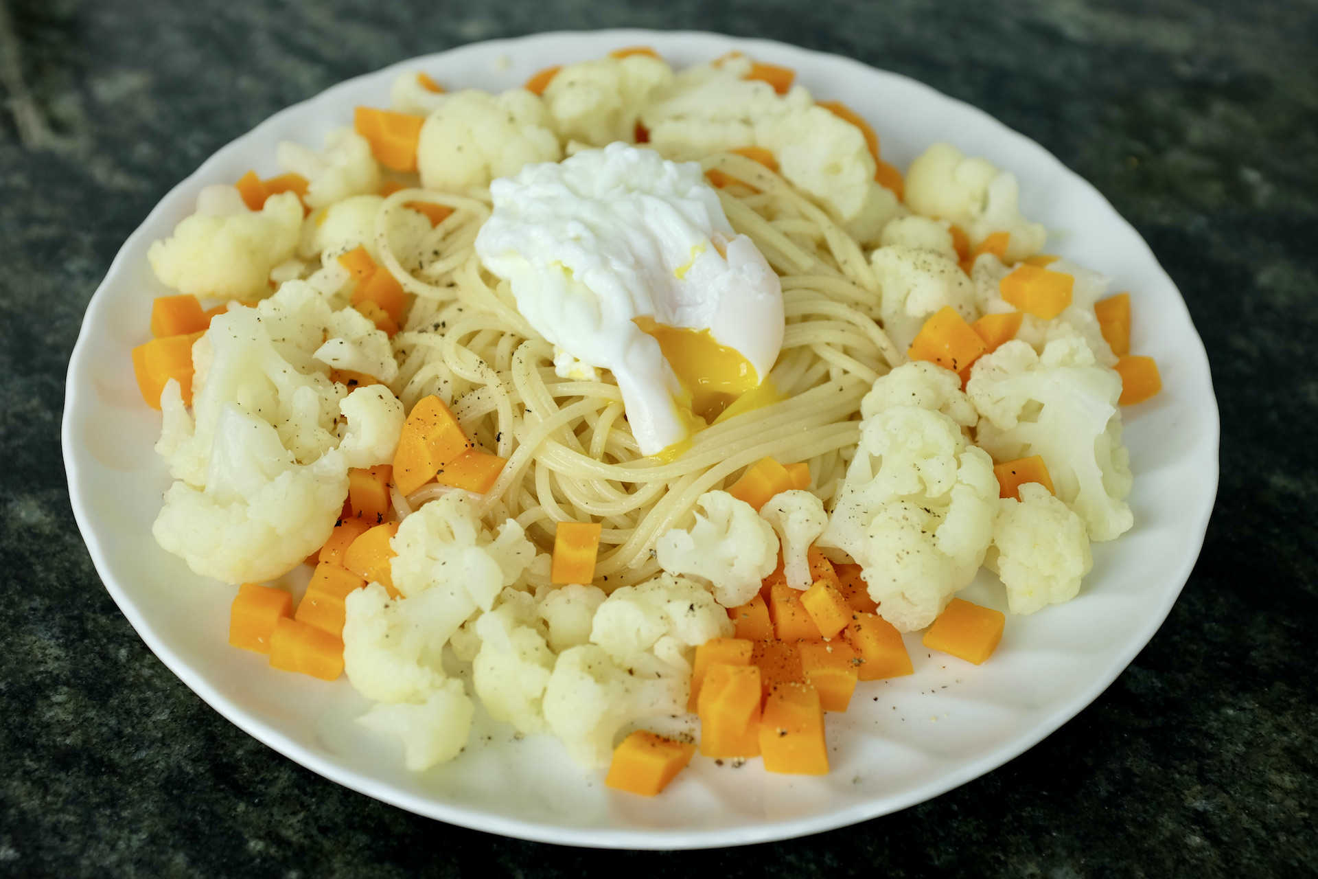 spaghetti pasta with vegetables a poached egg and freshly grounded black pepper