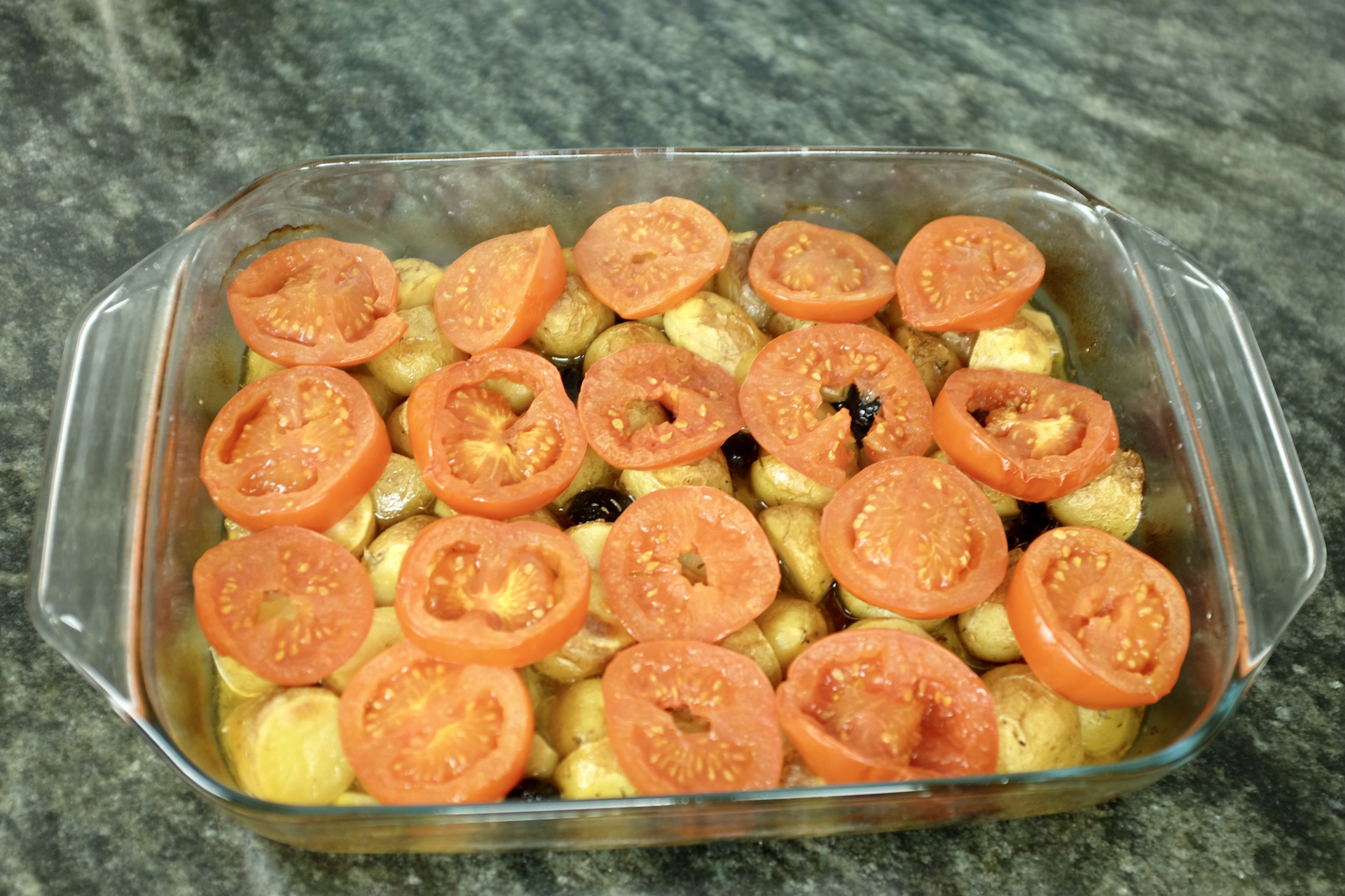 baby potatoes with tomato slices black olives and cloves of garlic baked in the oven