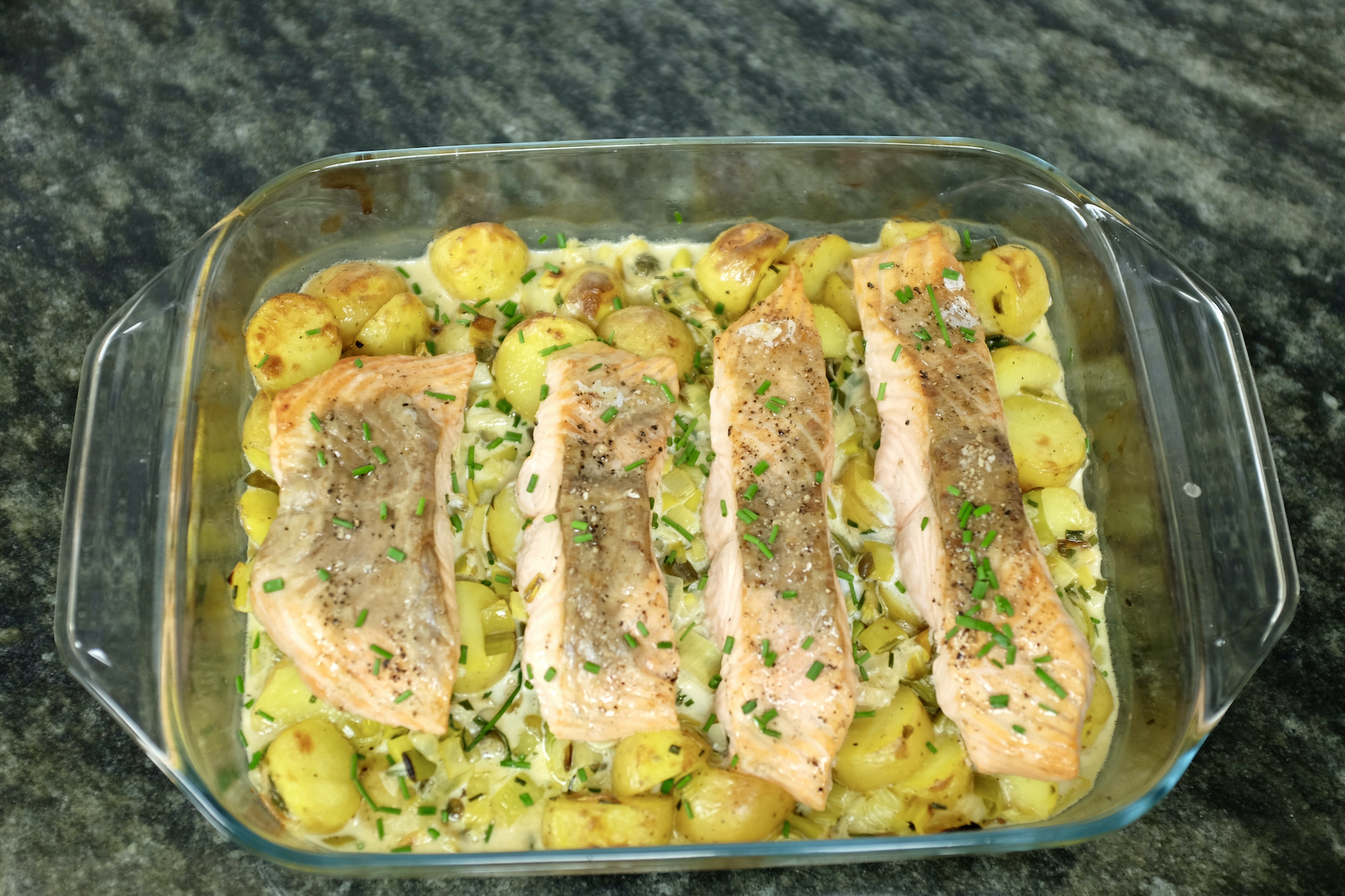 creamy salmon on a bed of baby potatoes leeks garlic and chives baked in the oven