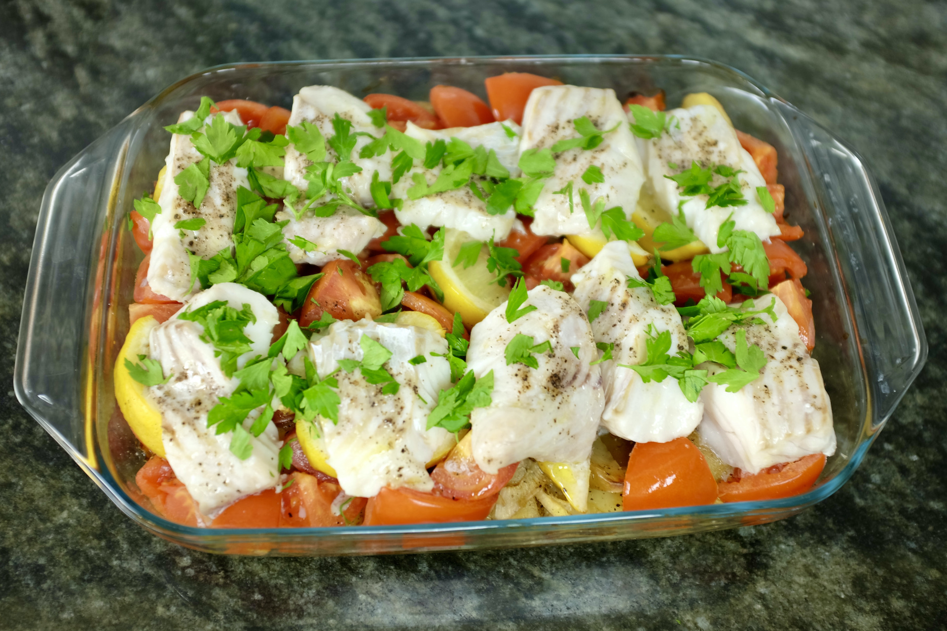 roasted fish greek style on a bed of potatoes onions lemon and tomatoes